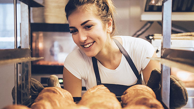 Mulher jovem sorridente verificando bandeja de pães tipo croissant.