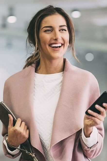 Mulher jovem elegante e sorridente segurando celular.